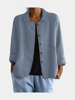 Open blouse in dusty blue with a crinkled weave and slanted hip pockets, worn over a black top